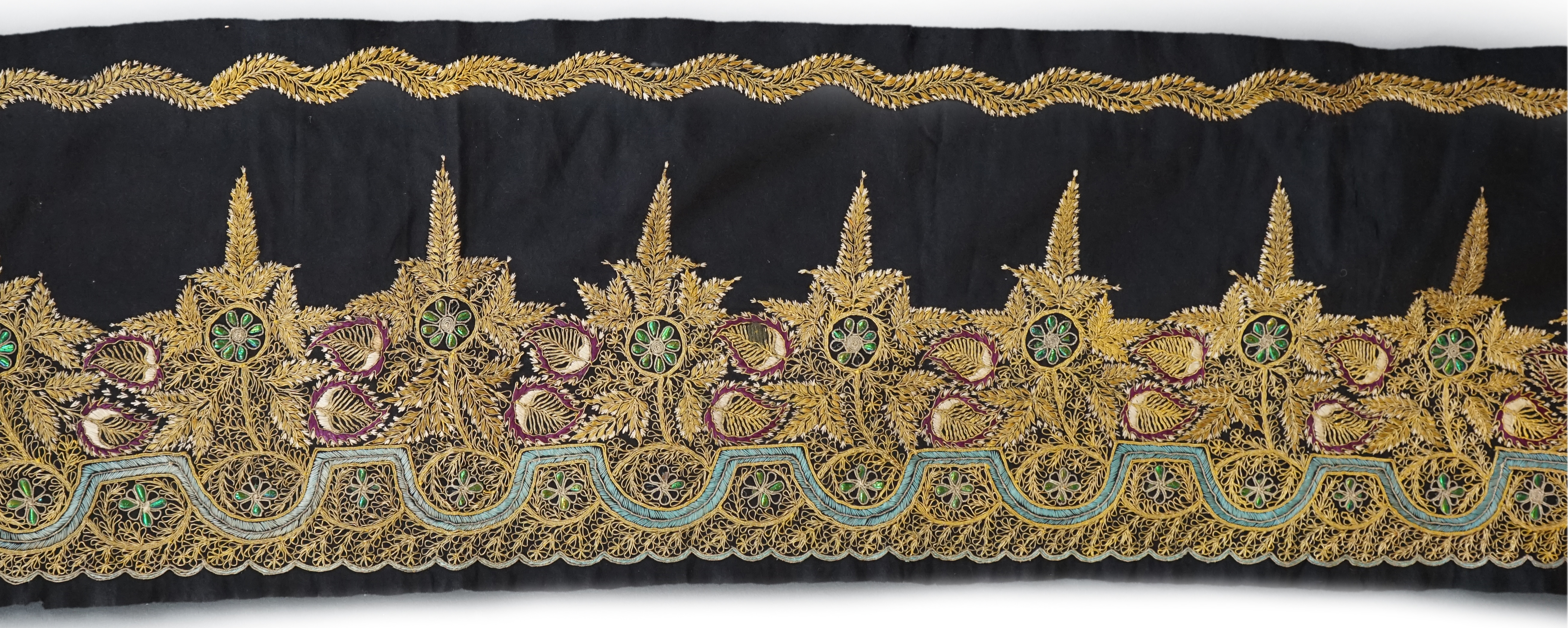 An Indian black felt panel embroidered with mostly gold thread, some coloured silks and beetle wing ornamentation, possibly a border to a larger panel, 256cm long. Condition - good